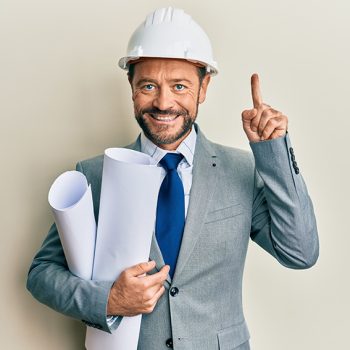 Middle age architect man wearing safety helmet holding blueprints smiling with an idea or question pointing finger with happy face, number one